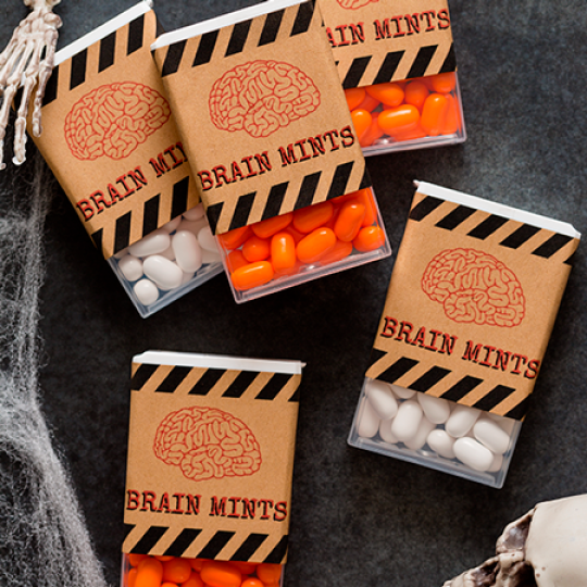 Halloween-klistermÀrke pÄ brun förpackning med en hjÀrnillustration, fylld med vita och orange pastiller pÄ en mörk yta.