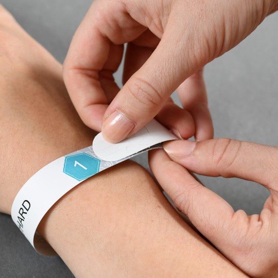 Självhäftande entréarmband fästs runt en handled.