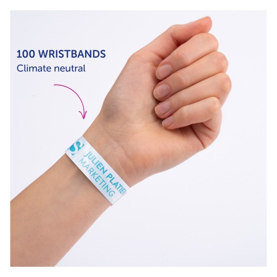 Bilden visar en persons hand med ett armband där det står '100 WRISTBANDS Klimatneutral' med 'JULIEN PLATTER MARKETING' tryckt på det.