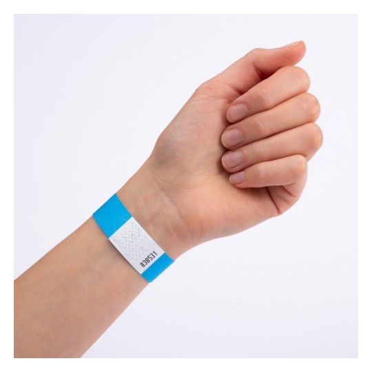 Bilden visar en hand som bär ett blått och vitt armband. Armbandet har en kod tryckt på det, vilket möjligtvis indikerar inträde eller åtkomst till ett evenemang.