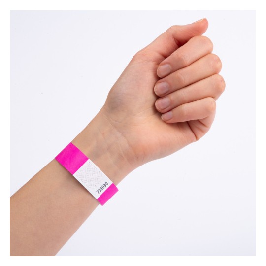 Bilden visar en hand med ett rosa armband som har en vit etikett och ett nummer tryckt på det. Handen är placerad med fingrarna stängda och armbandet är tydligt synligt.