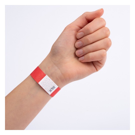 En hand som bär ett rött armband med en vit etikett som har sicksackmönster och tryckta siffror på.