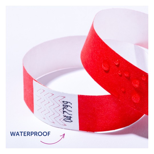 Bilden visar ett rött vattentätt armband med vattendroppar på. Det finns sicksackmönster och text på en vit remsa av armbandet.