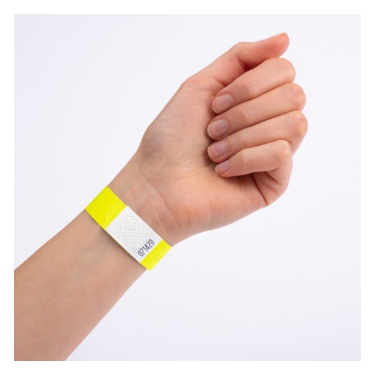 Denna bild visar en hand som bär ett gult armband med en vit sektion som har ett sicksackmönster och ett nummer på det.