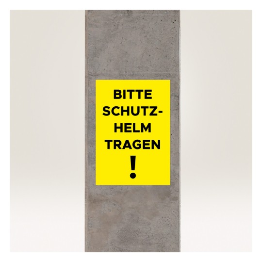 Bilden visar en gul skylt på en betongpelare med texten 'BITTE SCHUTZ-HELM TRAGEN!' vilket översätts till 'Var vänlig bär hjälm!' och anger ett säkerhetskrav.