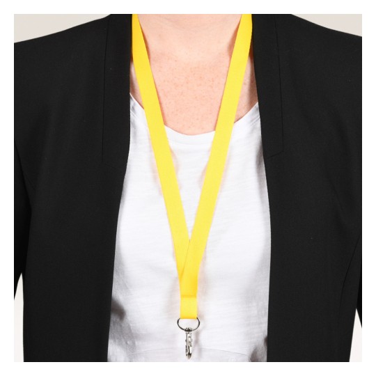 Bilden visar en person som bär en svart blazer över en vit skjorta, med ett ljust gult nyckelband som hänger runt halsen, vilket har en klämma fäst vid sig.
