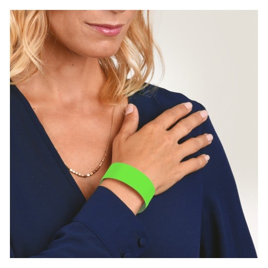 Bilden visar en kvinna som bär en marinblå blus och ett grönt armband på handen. Hon håller handen mot axeln, och hennes hår är stylat i lösa vågor. Bakgrunden är en ljus gradient.
