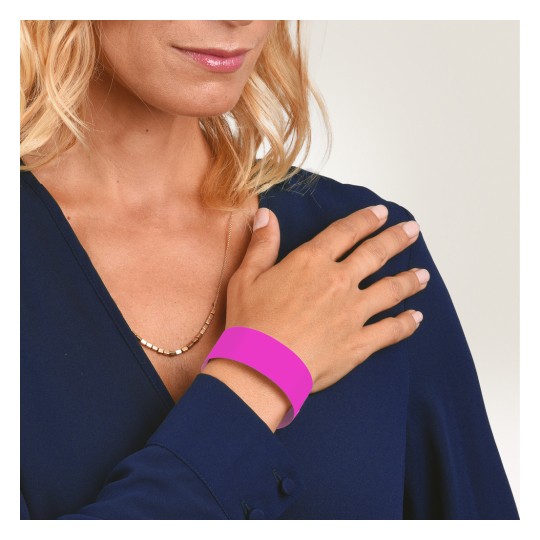 Bilden visar en kvinna som bär en mörkblå blus, och hon visar sin hand med ett rosa armband. Hon har blont, vågigt hår och vilar försiktigt sin hand på axeln.