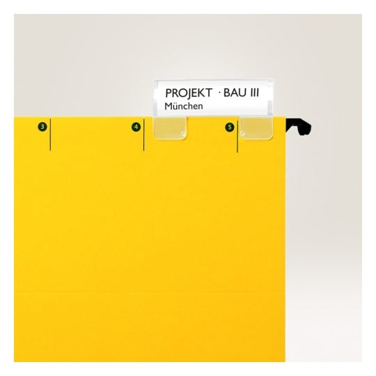Bilden visar en ljusgul mapp med en etiketthållare där det står 'PROJEKT · BAU III' och 'München'. Mappen har numeriska markörer på sidan.