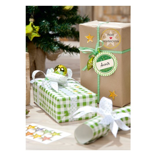 Bilden visar julklappar inslagna i dekorativt papper, med en liten julgran i bakgrunden. Paketen har gröna och vita mönster, och ett av dem är märkt 'Anna'. Det finns guldfärgade dekorationer och en stjärna på paketen, vilket skapar en festlig atmosfär.