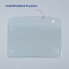 Bilden visar en klar, transparent plastkortshållare med rundade kanter och hål för fastsättning upptill. Den saknar något insatt innehåll och är placerad mot en grå bakgrund.