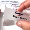 Bilden visar en hand som håller en namnskylt med texten 'Avery Paul Meyer.' Den framhäver hur enkelt det är att ta loss skylten, med betoning på de släta kanterna.