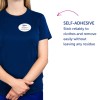 Bilden visar en person som bär en marinblå skjorta med en namnskylt som lyder 'B. Carlos, marknadschef.' Bredvid dem finns text som beskriver en självhäftande funktion som fäster på kläder och enkelt avlägsnas utan att lämna rester.