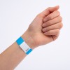 Bilden visar en hand som bär ett blått och vitt armband. Armbandet har en kod tryckt på det, vilket möjligtvis indikerar inträde eller åtkomst till ett evenemang.