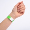 En närbild av en hand med ett grönt armband på handleden. Armbandet har en vit sektion med ett sicksackmönster och verkar vara märkt med ett nummer.