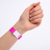 Bilden visar en hand med ett rosa armband som har en vit etikett och ett nummer tryckt på det. Handen är placerad med fingrarna stängda och armbandet är tydligt synligt.