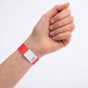 En hand som bär ett rött armband med en vit etikett som har sicksackmönster och tryckta siffror på.