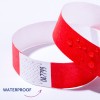 Bilden visar ett rött vattentätt armband med vattendroppar på. Det finns sicksackmönster och text på en vit remsa av armbandet.