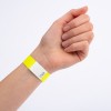 Denna bild visar en hand som bär ett gult armband med en vit sektion som har ett sicksackmönster och ett nummer på det.