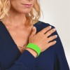 Bilden visar en kvinna som bär en marinblå blus och ett grönt armband på handen. Hon håller handen mot axeln, och hennes hår är stylat i lösa vågor. Bakgrunden är en ljus gradient.