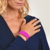 Bilden visar en kvinna som bär en mörkblå blus, och hon visar sin hand med ett rosa armband. Hon har blont, vågigt hår och vilar försiktigt sin hand på axeln.